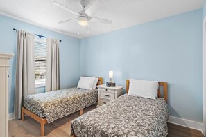 Ein Schlafzimmer mit zwei Betten, einem Deckenventilator, einem Nachttisch mit Lampe und einem Fenster mit Jalousien.