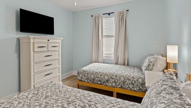 Een slaapkamer met twee bedden, een dressoir, een plafondventilator en een televisie.