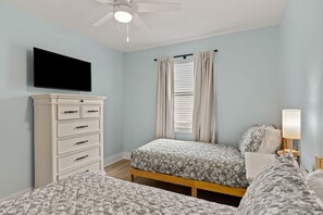 Une chambre avec deux lits, une commode, un ventilateur de plafond et un téléviseur.