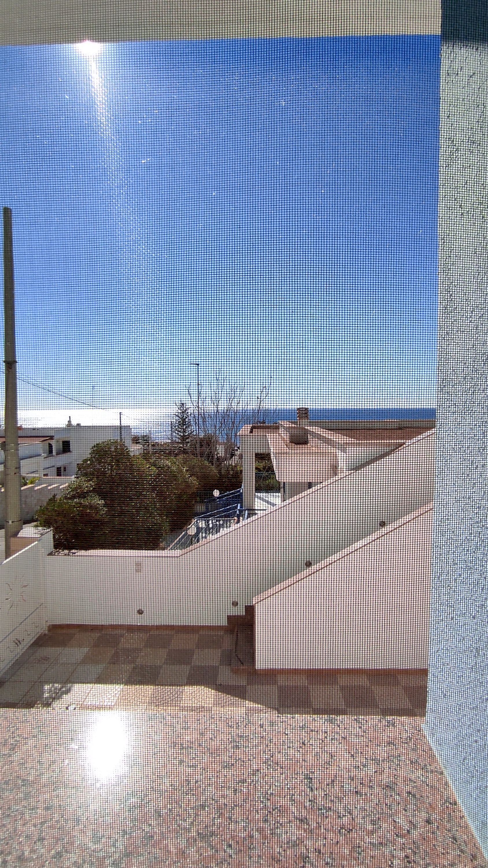 Un balcon avec vue sur la mer, un sol carrelé et un mur blanc.