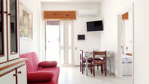 Ein geräumiger Wohnbereich mit einem roten Sofa, einem Esstisch mit Stühlen, einem an der Wand befestigten Fernseher und einer Küche im Hintergrund.