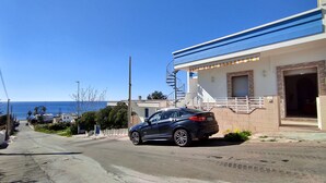 Eine Küstenstraße mit einem geparkten Auto, einem Gebäude mit blauem Markisen und freiem Blick auf das Meer.