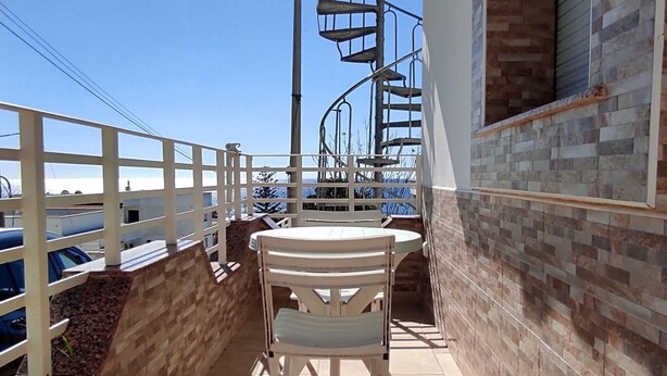 Ein Balkon mit einem weißen Stuhl, einer Wendeltreppe und Blick auf das Meer.