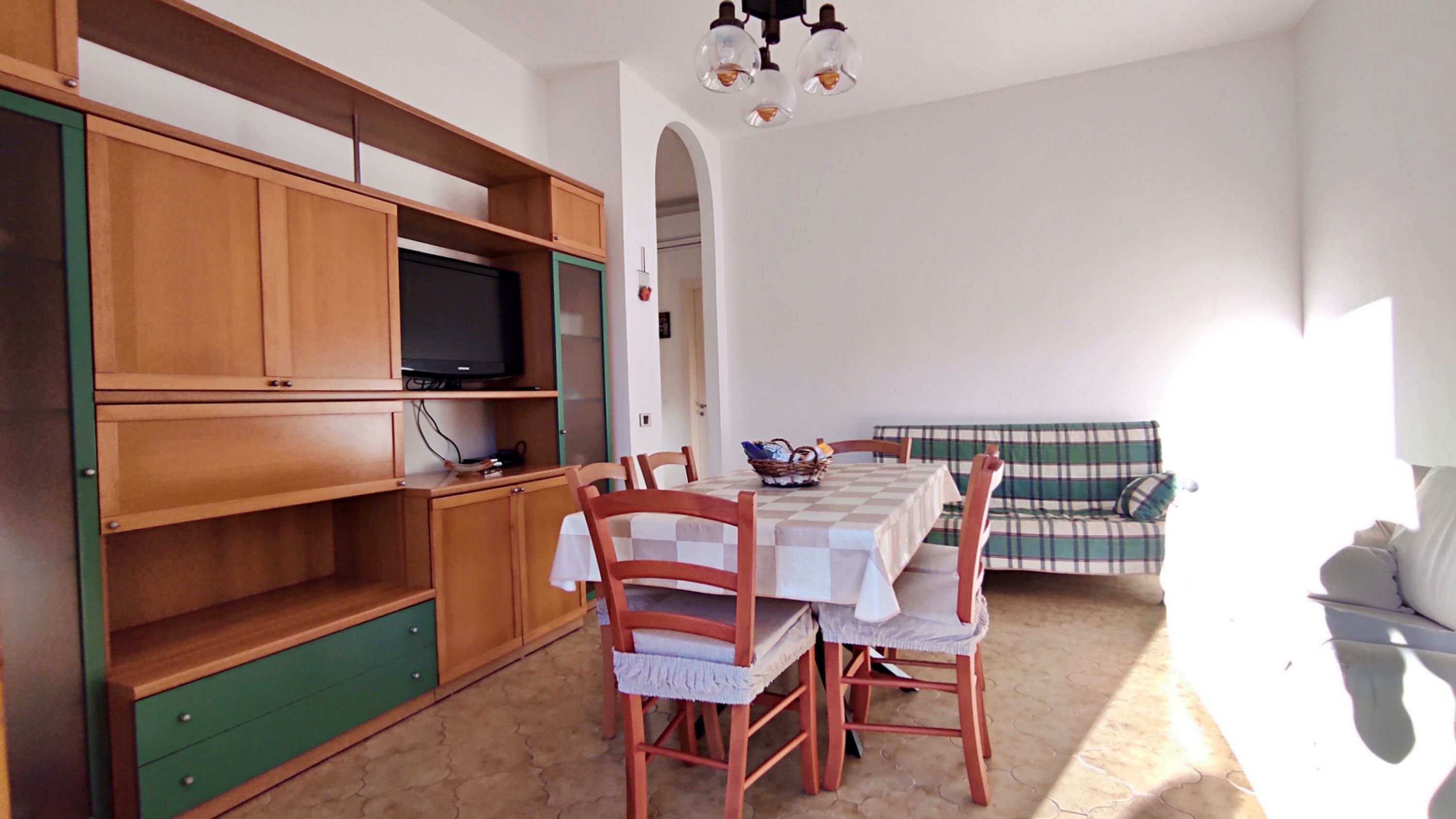 A room with a dining table, chairs, a television on a shelf, and a sofa.
