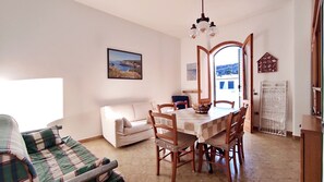 Ein Wohnzimmer mit Sofa, Esstisch mit Stühlen, einem Bild an der Wand und Blick durch eine offene Tür.