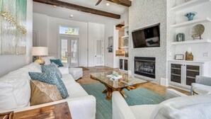 A spacious living room with a fireplace, a ceiling fan, and a TV mounted on the wall. - Marlin Haven @ Holiday Isle (Destin)