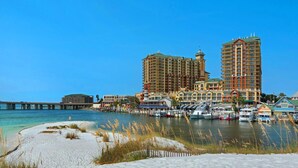 A beachfront hotel with multiple high-rise buildings, a pier, and boats docked near the shore. - Marlin Haven @ Holiday Isle (Destin)