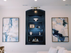 A room with a central dark blue shelving unit displaying various items, flanked by abstract paintings on the walls.