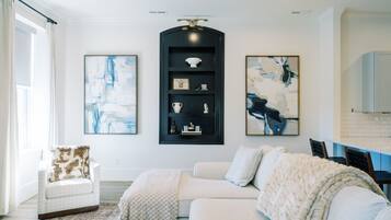 A modern living room with a white sofa, a black shelving unit, and abstract paintings.