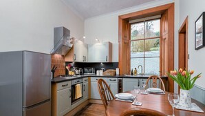 A modern kitchen with stainless steel appliances, wooden cabinets, and a dining area with a table set for two. - The Cosy Nook - Free Parking Nearby (Dunblane)