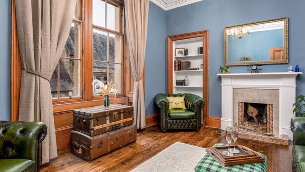 A room with a fireplace, a green armchair, a wooden chest of drawers, and a bookshelf. - The Cosy Nook - Free Parking Nearby (Dunblane)