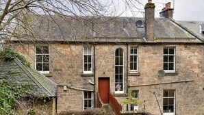 A stone building with a central door, multiple windows, and a small garden area with a potted plant. - The Cosy Nook - Free Parking Nearby (Dunblane)
