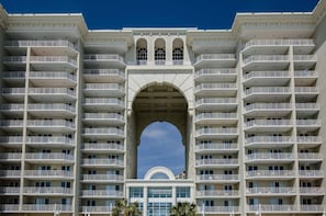 A multi-story hotel with balconies, a central archway, and a clear sky. - Majestic Sun 711b- 7th Heaven (Miramar Beach)