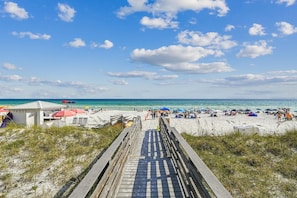 Ein Strand mit einer Holzpromenade, die zum Ufer führt, Sonnenschirmen und Strandbesuchern.