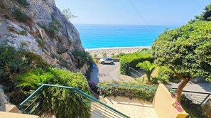 Un escalier qui descend vers une plage, avec une voiture garée sur la route.