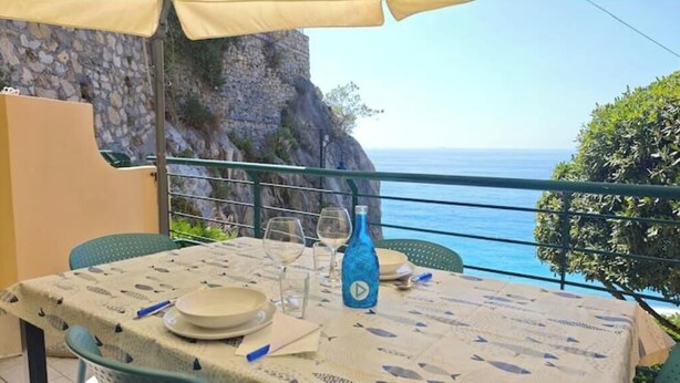 Mesa posta para refeição com vista para o mar, uma garrafa e uma cadeira.