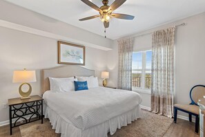 A bedroom with a bed, two bedside tables with lamps, a ceiling fan, a window with curtains, and a chair. - Majestic Sun 1108b - Wave Whisper (Miramar Beach)