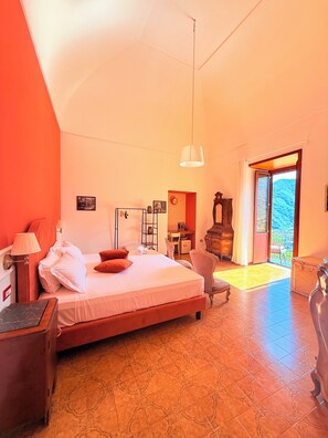 Un dormitorio con cama, escritorio, silla, lámpara y vistas al exterior.