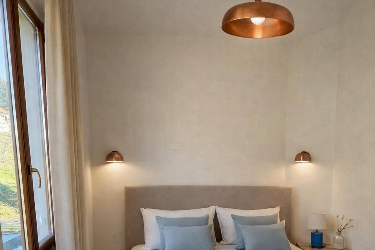 A bedroom with a bed, a window, curtains, a hanging light fixture, and bedside lamps.
