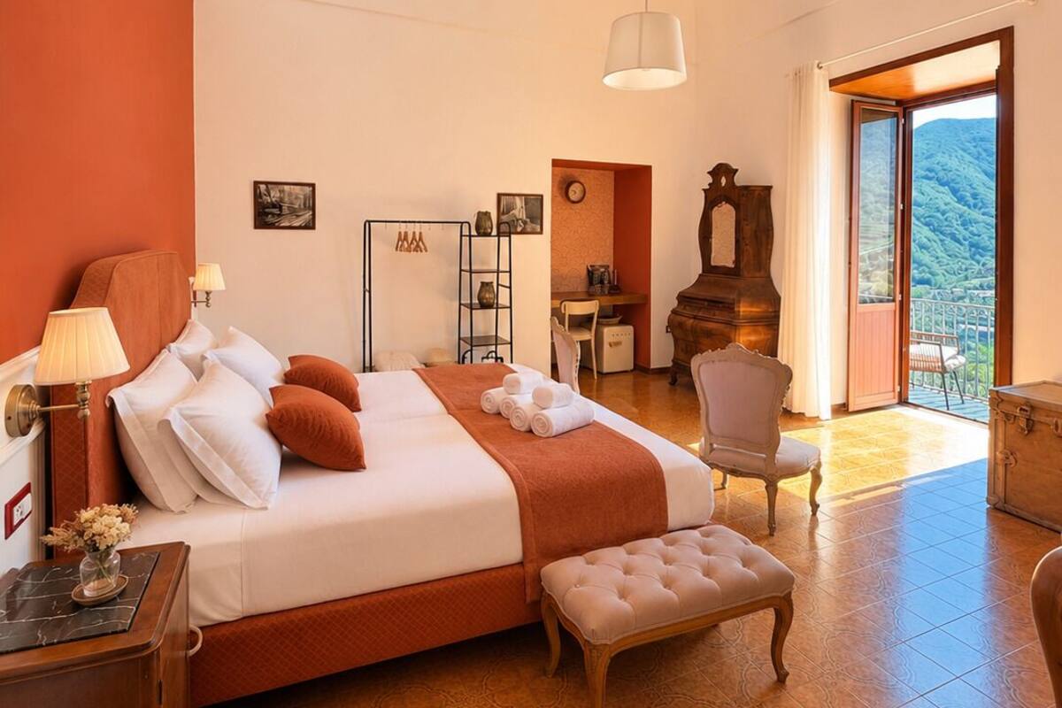 A spacious bedroom with a large bed, a desk, and a view of a mountainous landscape.