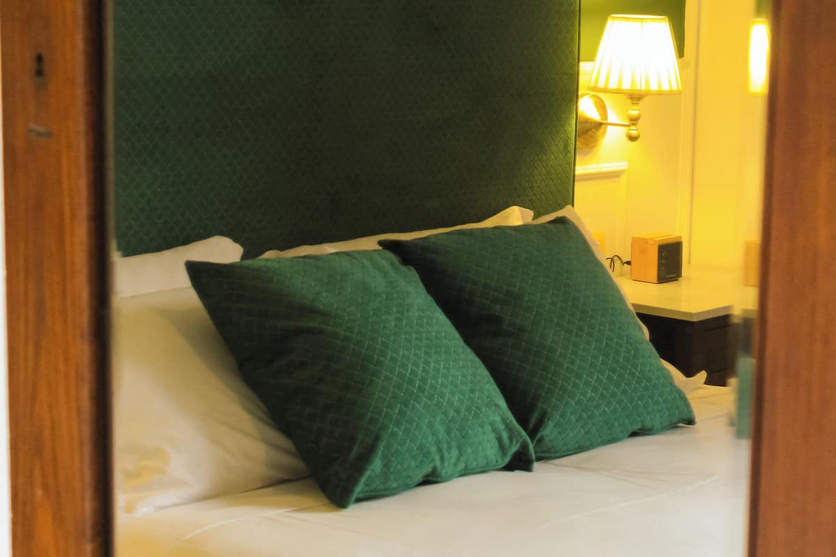 A bed with green pillows and a headboard, a bedside table with a lamp, and a nightstand with a radio.