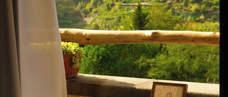A balcony with a table, chairs, a potted plant, and a scenic view of a valley with buildings.