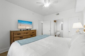 A bedroom with a bed, a dresser, a ceiling fan, a TV, and a bathroom visible through an open door. - Majestic Sun 314a- Vista Esmeralda (Miramar Beach)