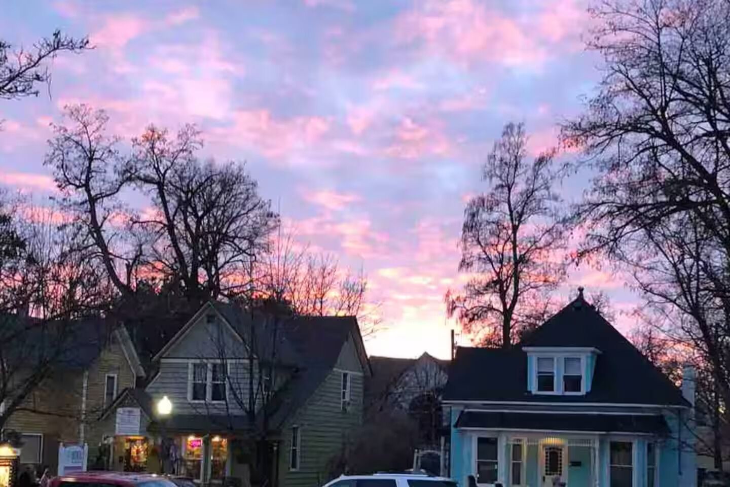 Una calle residencial con casas, árboles y un cielo al atardecer.