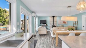 Eine moderne Küche mit großem Fenster, ein Essbereich mit Tisch und Stühlen sowie ein Wohnzimmer mit Sofa und Fernseher.
