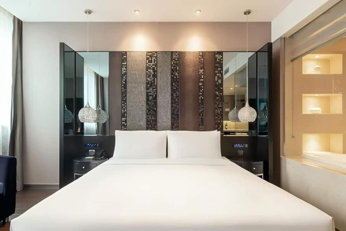 A modern hotel room with a large bed, bedside tables, a mirror, and pendant lighting.