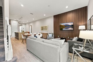 A modern living room with a grey sofa, a dining area with a wooden table, and a kitchen with white cabinets. - Family Retreat with 4Bed suites & Private Jacuzzi (Four Corners)