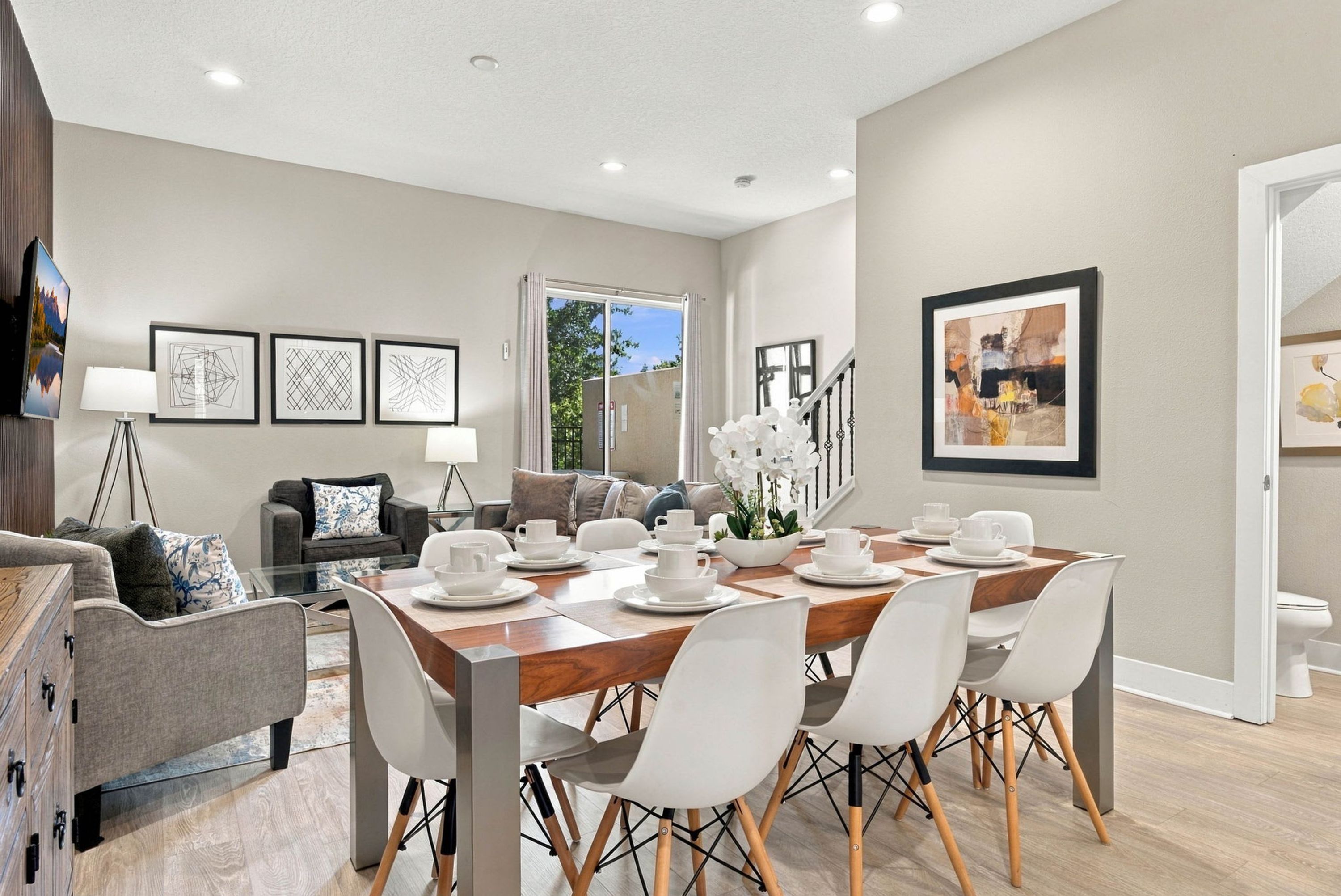 Un espace repas moderne avec une table en bois dressée pour quatre personnes, entourée de chaises blanches.