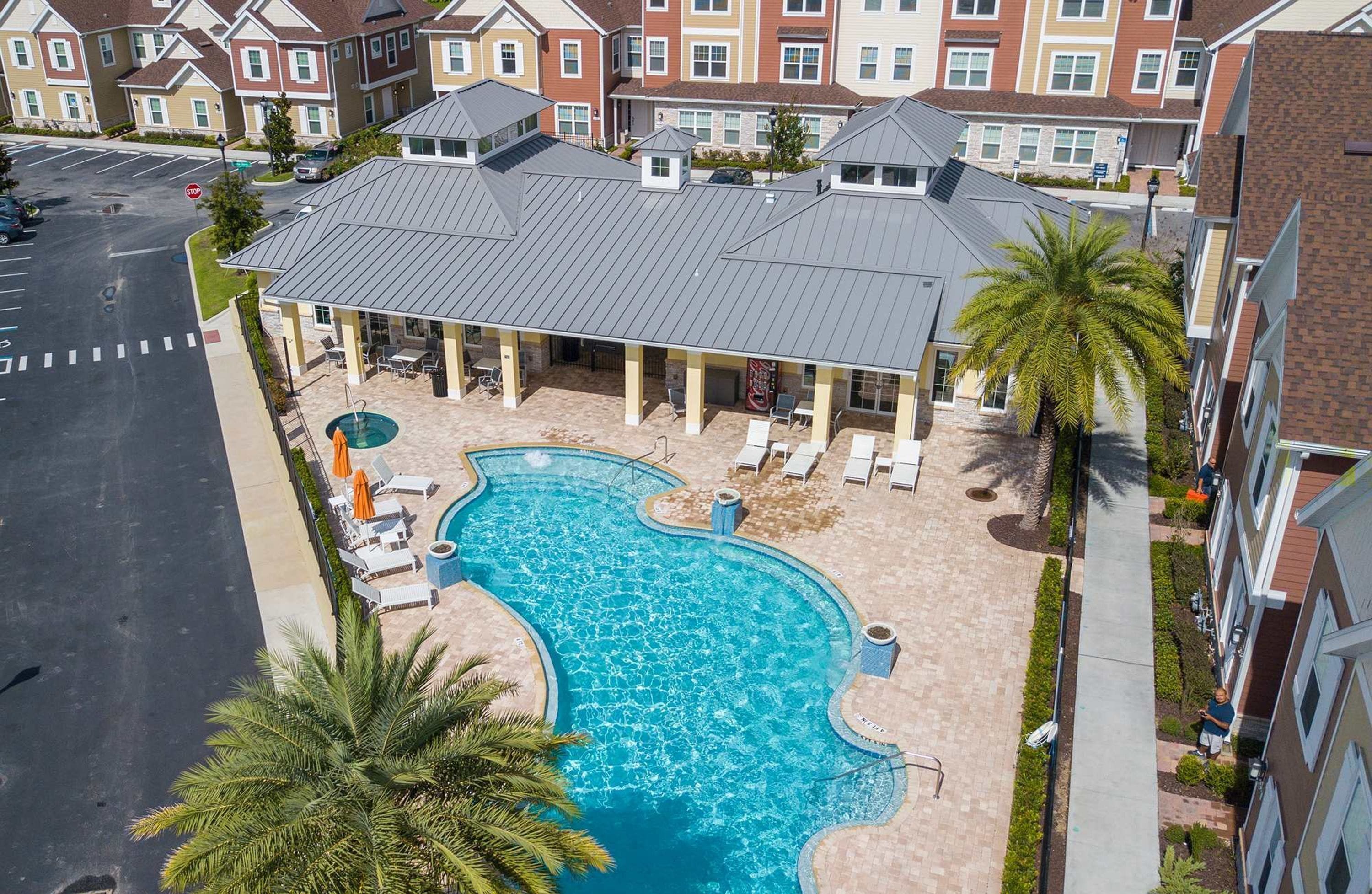 A residential building with a swimming pool, lounge chairs, and palm trees.