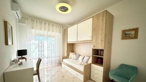 Ein Zimmer mit Bett, Schreibtisch, Stuhl, Fernseher und einem fenster mit Vorhängen.