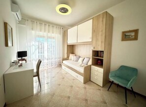 A room with a bed, a desk, a chair, a TV, and a window with curtains. - Hostdomus - Ela House (Finale Ligure)