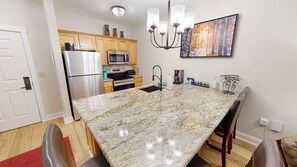 A kitchen with granite countertops, a stainless steel refrigerator, a microwave, and a chandelier. - NEW! Seneca 213 - Brigham One Bedroom Plus Condo (Snowshoe)