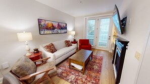 A living room with a sofa, armchair, coffee table, TV, and artwork on the wall. - NEW! Seneca 213 - Brigham One Bedroom Plus Condo (Snowshoe)