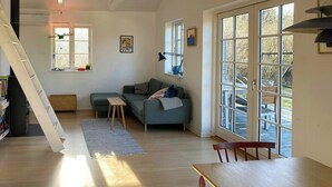 Una sala de estar con sofá, una mesa de madera, una escalera y ventanas grandes.