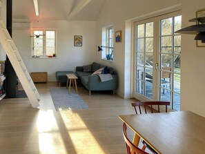 Ein Wohnzimmer mit einer Couch, einem Holztisch, einer Treppe und großen Fenstern.