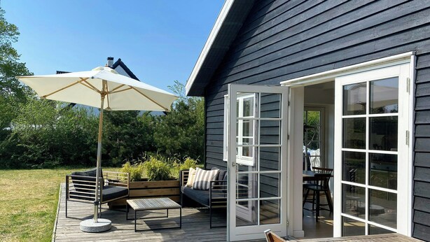 Una terraza con mobiliario exterior, una mesa y un paraguas grande.