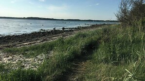 Un paisaje costero con una playa arenosa, zonas verdes y una masa de agua tranquila.