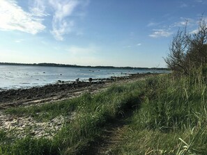 Eine Küstenlandschaft mit Sandstrand, Grünflächen und ruhigem Gewässer.