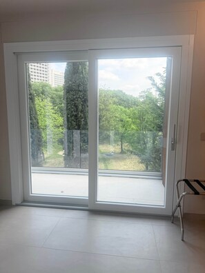 Habitación con un gran ventanal corredero que da a un espacio exterior con vista a árboles y una hamaca.