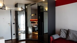 Moderni hotellihuone, jossa on peilipintainen vaatekaappi, punainen sohva ja puulattia.
