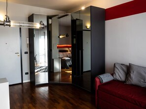 A modern hotel room with a mirrored wardrobe, a red sofa, and a wooden floor. - CARLOTTA STATION SUITE (Bologna)