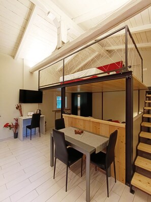 Un habitación estilo loft con comedor, una pequeña cocina y una escalera.