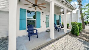 Eine überdachte Veranda mit zwei blauen Stühlen, einem Deckenventilator und einer Palme.
