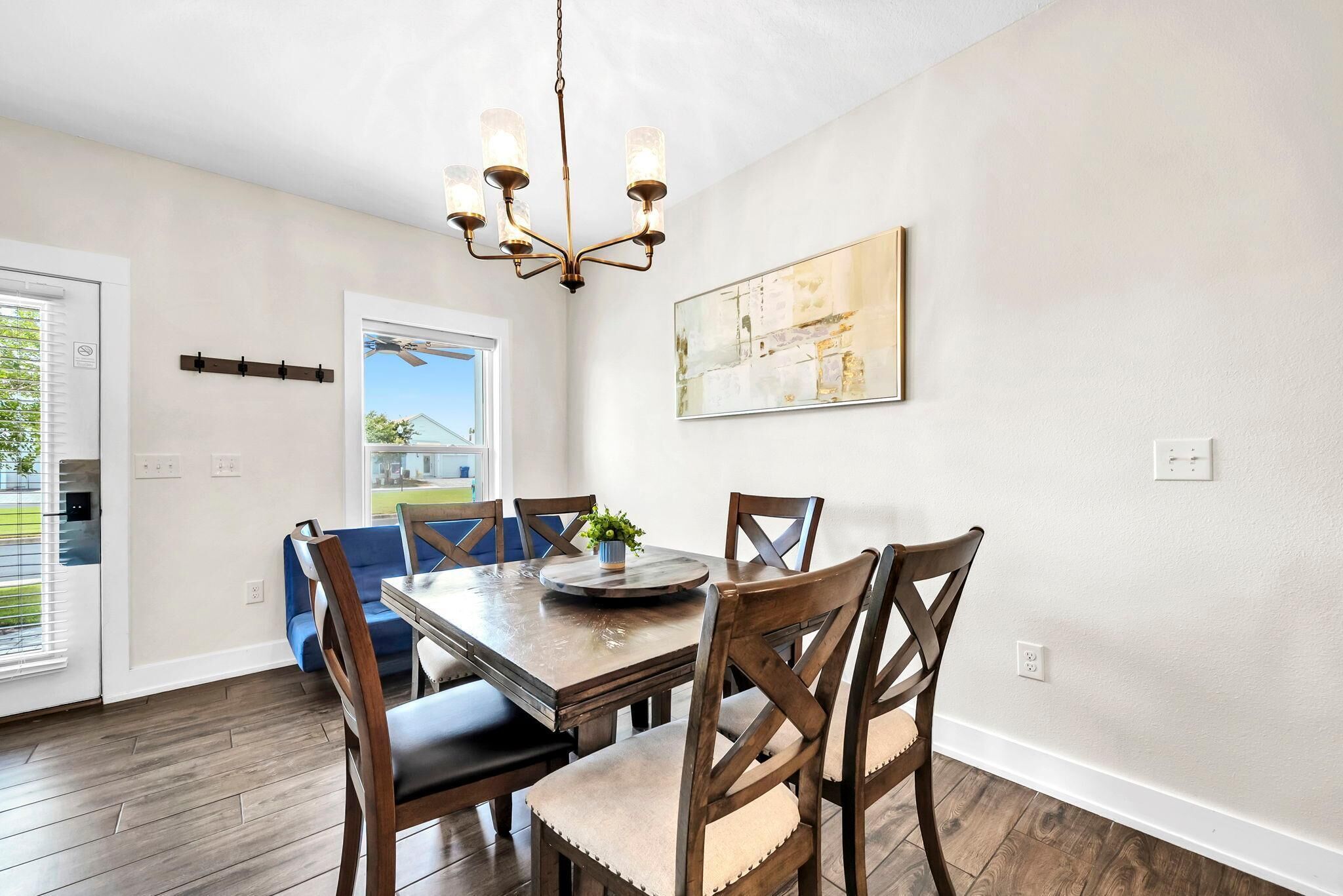 Un coin repas avec une table en bois, six chaises, un lustre et un tableau accroché au mur.