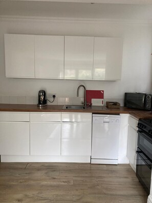 A kitchen with white cabinets, a dishwasher, a coffee maker, a microwave, and a stove.