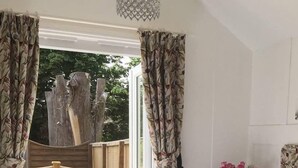 A bedroom with a bed, a small table with chairs, a vase with flowers, and a view of the outdoors. - Clarence House Holidays (Shanklin)